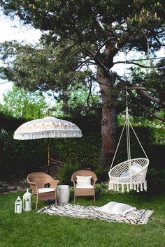 two chairs and an umbrella are sitting in the grass near a tree with a blanket on it