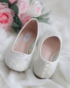 a pair of white wedding shoes sitting on top of a bed next to pink roses