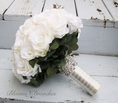 a bridal bouquet with white roses and greenery on the side of a wooden bench