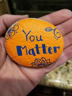 a hand holding an orange with the words you matter written on it in blue ink