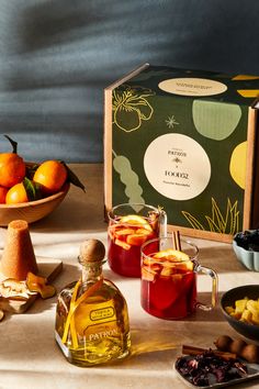 an assortment of fruits and drinks on a table with a box of oranges in the background