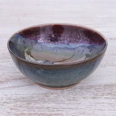 a purple and green bowl sitting on top of a wooden table next to a white wall