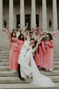 a bride and groom kissing on the steps of a building with their bridal party