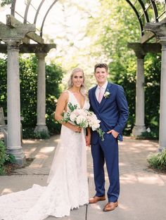 a bride and groom pose for a wedding photo in front of an arbor with greenery