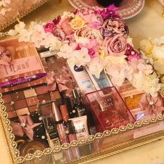 an assortment of beauty products displayed in a gold framed tray on a table with pink and white flowers