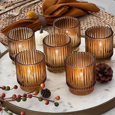 four glasses on a table with pine cones and other decorations around it, including a candle holder