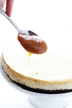 a person spooning caramel sauce onto a cheesecake on a white cake plate