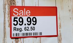 a red and white sale sign hanging on the side of a wooden wall with peeling paint