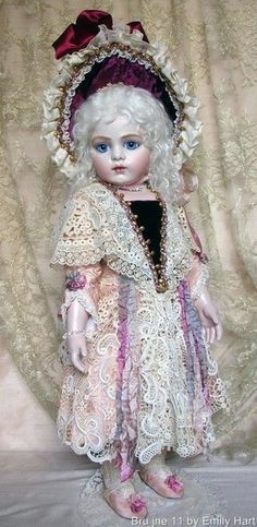 a doll with white hair and blue eyes wearing a pink dress is standing in front of a curtain