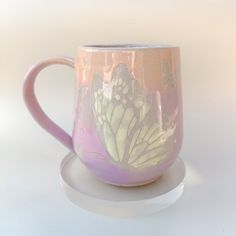 a pink coffee cup with a butterfly painted on it sitting on a white table top