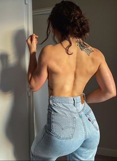 a woman standing in front of a mirror with her back turned to the camera and wearing jeans