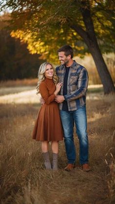 a man and woman standing next to each other in a field with trees behind them