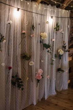 flowers are hanging on the wall in front of sheer curtains with lights strung from them