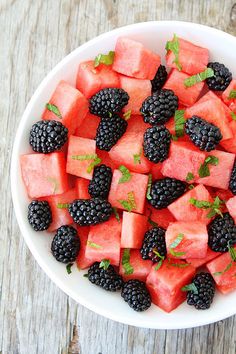 a white bowl filled with watermelon and blackberries on top of a wooden table