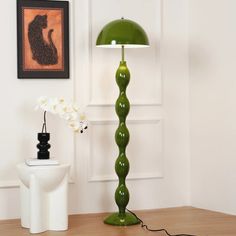 a green lamp sitting on top of a wooden table next to a white vase with flowers