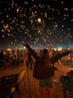 a woman is standing in the sand with her arms up and lights flying above her