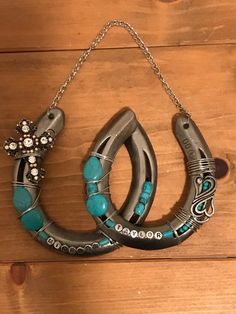 a pair of silver horseshoes with turquoise beads hanging from a chain on a wooden surface