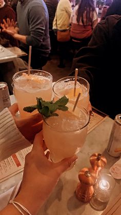 two people holding up drinks in front of each other at a table with menus on it