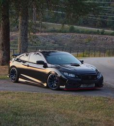 a black sports car parked on the side of a road next to trees and grass