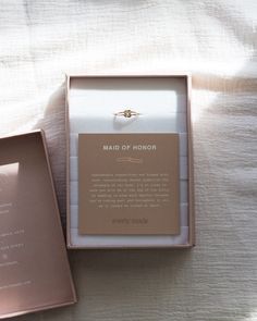 an open box with a ring inside on a white bed sheet, next to it's packaging