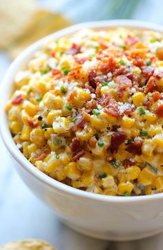 a bowl filled with corn and bacon on top of a table next to crackers