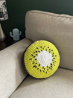 a yellow and white knitted cushion sitting on a couch next to a cactus plant