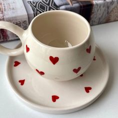 a cup and saucer with red hearts on it sitting next to a stack of books