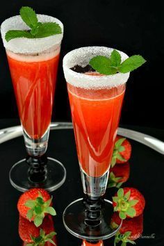 two glasses filled with liquid and strawberries on top of a black table next to each other