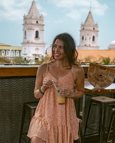 a woman holding a drink in her right hand and standing next to a table with chairs on it