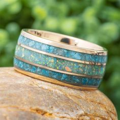 a gold and turquoise ring sitting on top of a rock in front of some trees