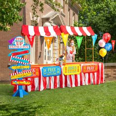 a child standing in front of a carnival booth with balloons and signs on the grass