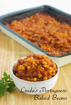 a white bowl filled with beans next to a baking pan full of baked beans and parsley