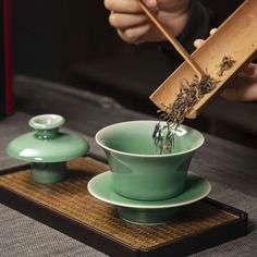 a person holding chopsticks over a green tea cup on top of a wooden tray