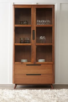 a tall wooden cabinet with glass doors and drawers on the bottom, in front of a white rug