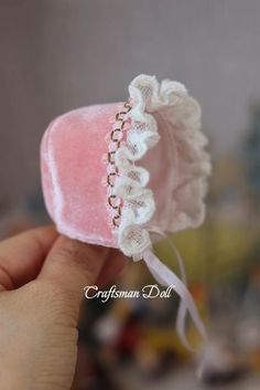 a hand holding a pink heart shaped object with white lace on the top and bottom