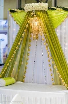 a white and green wedding setup with flowers on the headboard, drapes and lights in the background