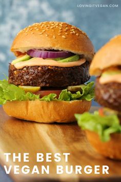 two hamburgers sitting on top of a wooden cutting board