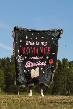 a woman standing in the grass holding a black blanket that says, this is my romance reading bluuleet