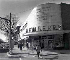 black and white photograph of people walking on the sidewalk in front of a newberry store