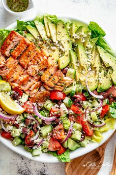 a salad with salmon, avocado, tomatoes and cucumber in it