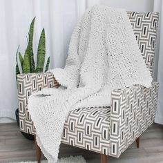 a chair with a blanket on it next to a potted plant