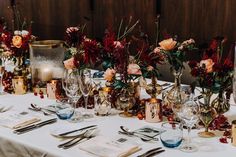 the table is set with wine glasses, silverware and floral centerpieces on it