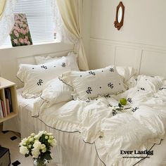 a white bed topped with lots of pillows next to a window