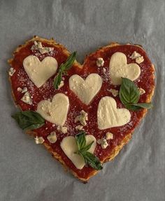 a heart shaped pizza topped with cheese and basil