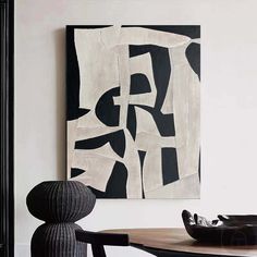 a black and white painting hanging on the wall next to a table with a vase