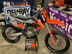 an orange and black dirt bike on display at a motorcycle shop with other items in the background