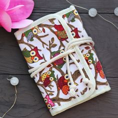 an owl themed notebook tied to a wooden table with pink flower in the background and white fabric wrapped around it