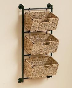 three wicker baskets are hanging on the wall next to an iron rack with wheels