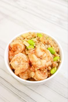 a bowl filled with rice and shrimp on top of a white countertop next to chopsticks