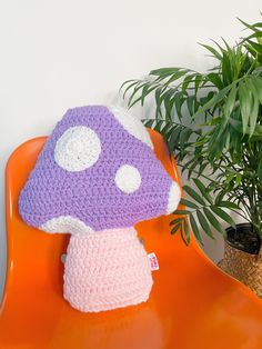 a crocheted mushroom hat sitting on an orange chair next to a potted plant